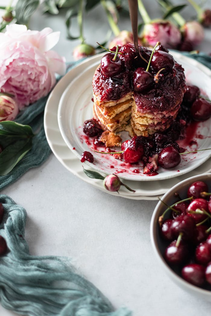 home-hero Delicious cherry-topped pancakes styled with peonies for a rustic brunch setting.